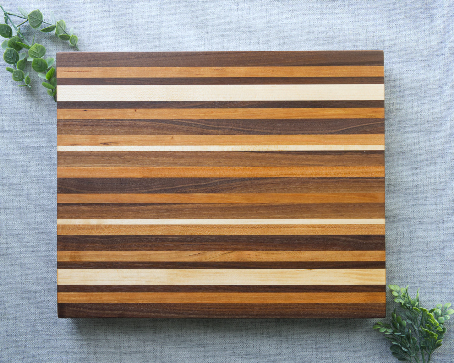 Pattern edge grain cutting board shown on grey table top. Top side of shown of cutting board made from domestic hardwoods: black walnut, cherry and hard maple.