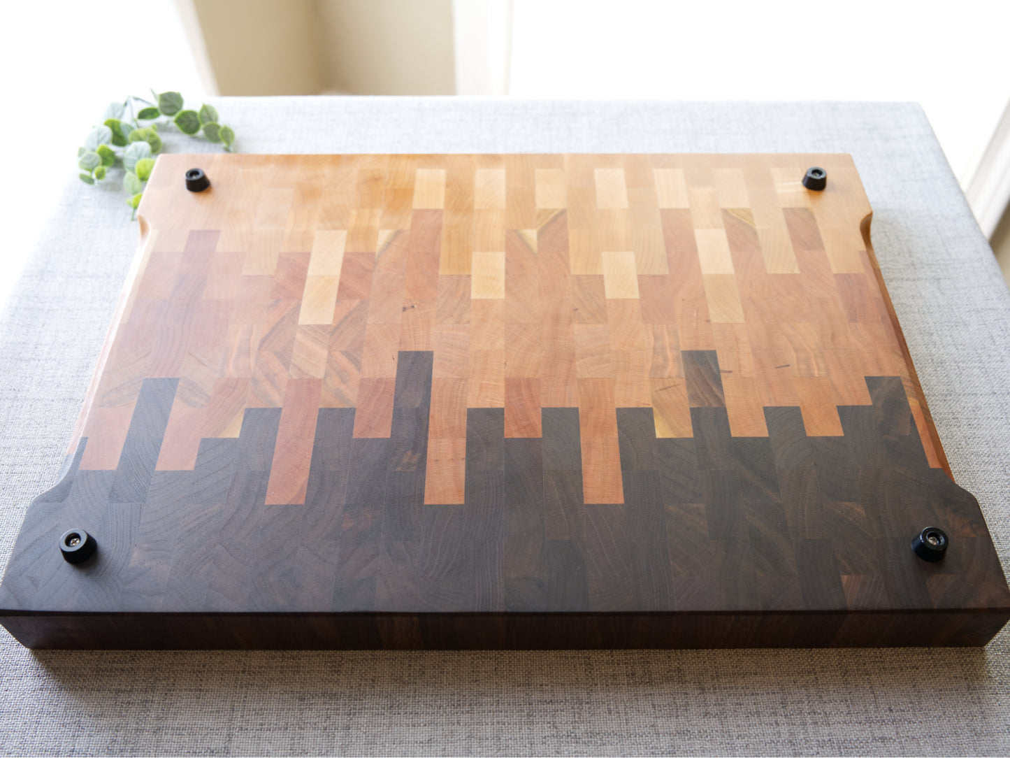 Ombre End Grain Cutting board made from domestic black walnut, maple and cherry. Shown on grey cloth table and is finished with mineral oil and beeswax. Bottom view shown with silicon feet