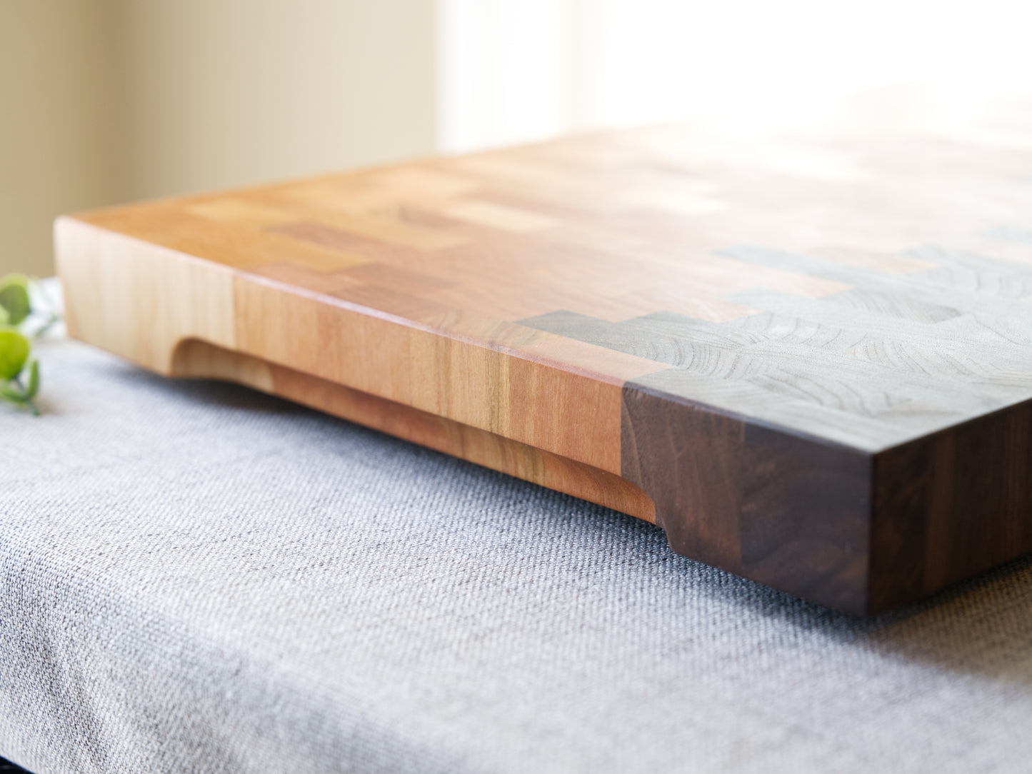 Ombre End Grain Cutting board made from domestic black walnut, maple and cherry. Shown on grey cloth table and is finished with mineral oil and beeswax. Side view is shown to detail the finger grooves