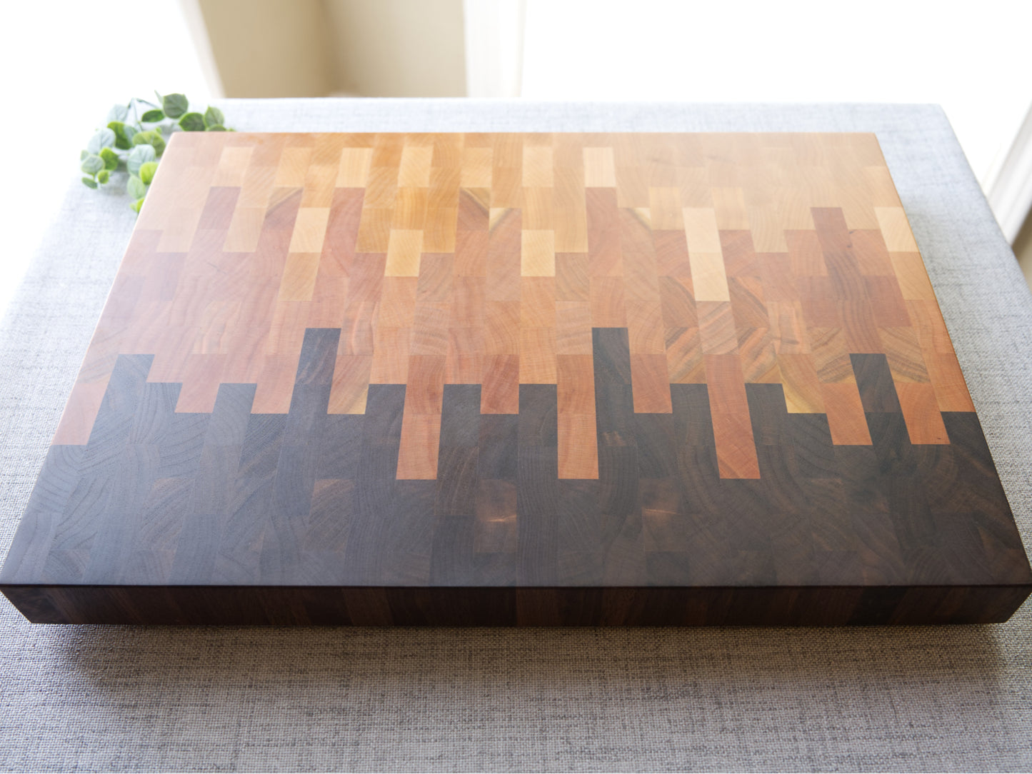 Ombre End Grain Cutting board made from domestic black walnut, maple and cherry. Shown on grey cloth table and is finished with mineral oil and beeswax. Angled top view shown