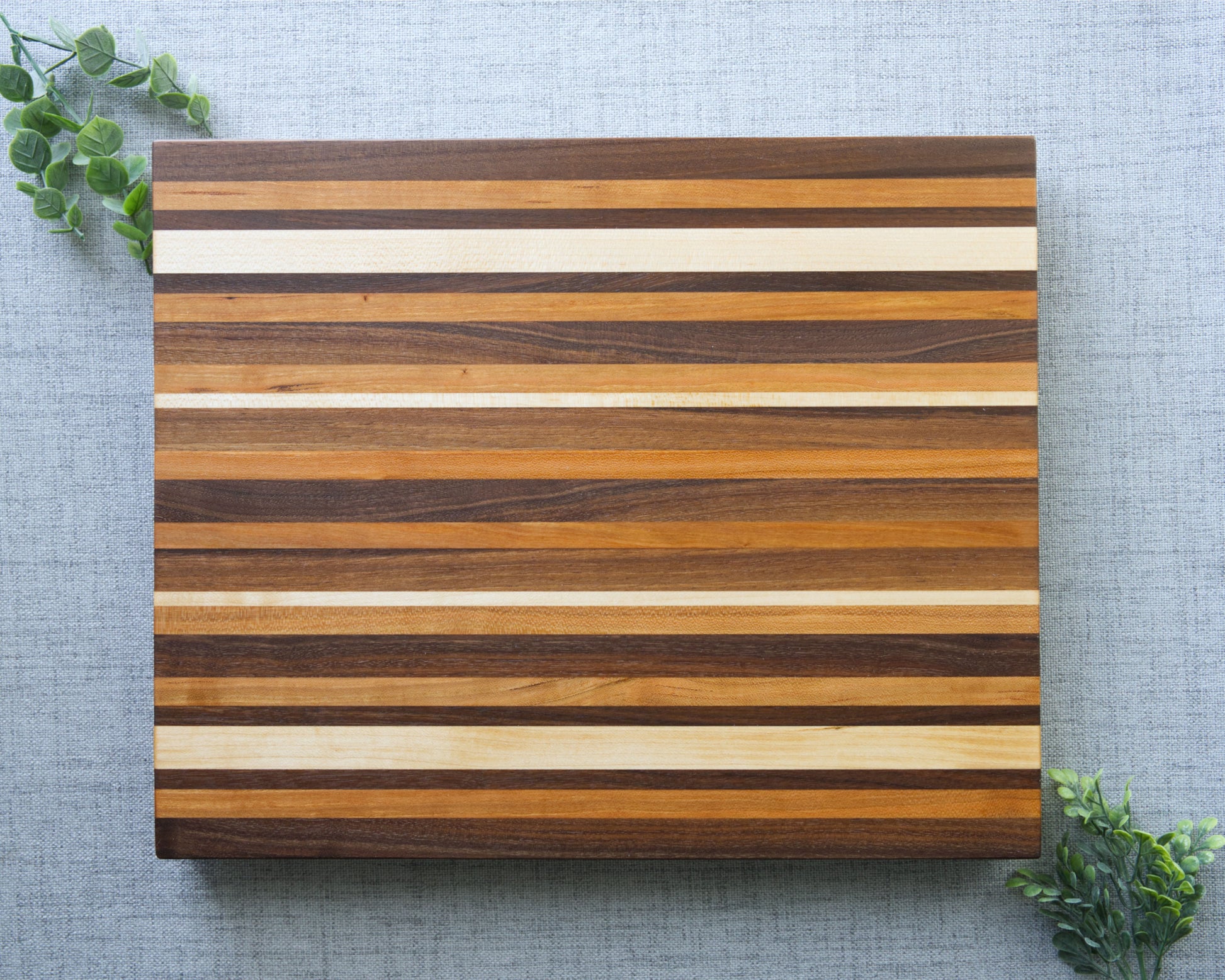 Pattern edge grain cutting board shown on grey table top. Top side of shown of cutting board made from domestic hardwoods: black walnut, cherry and hard maple.