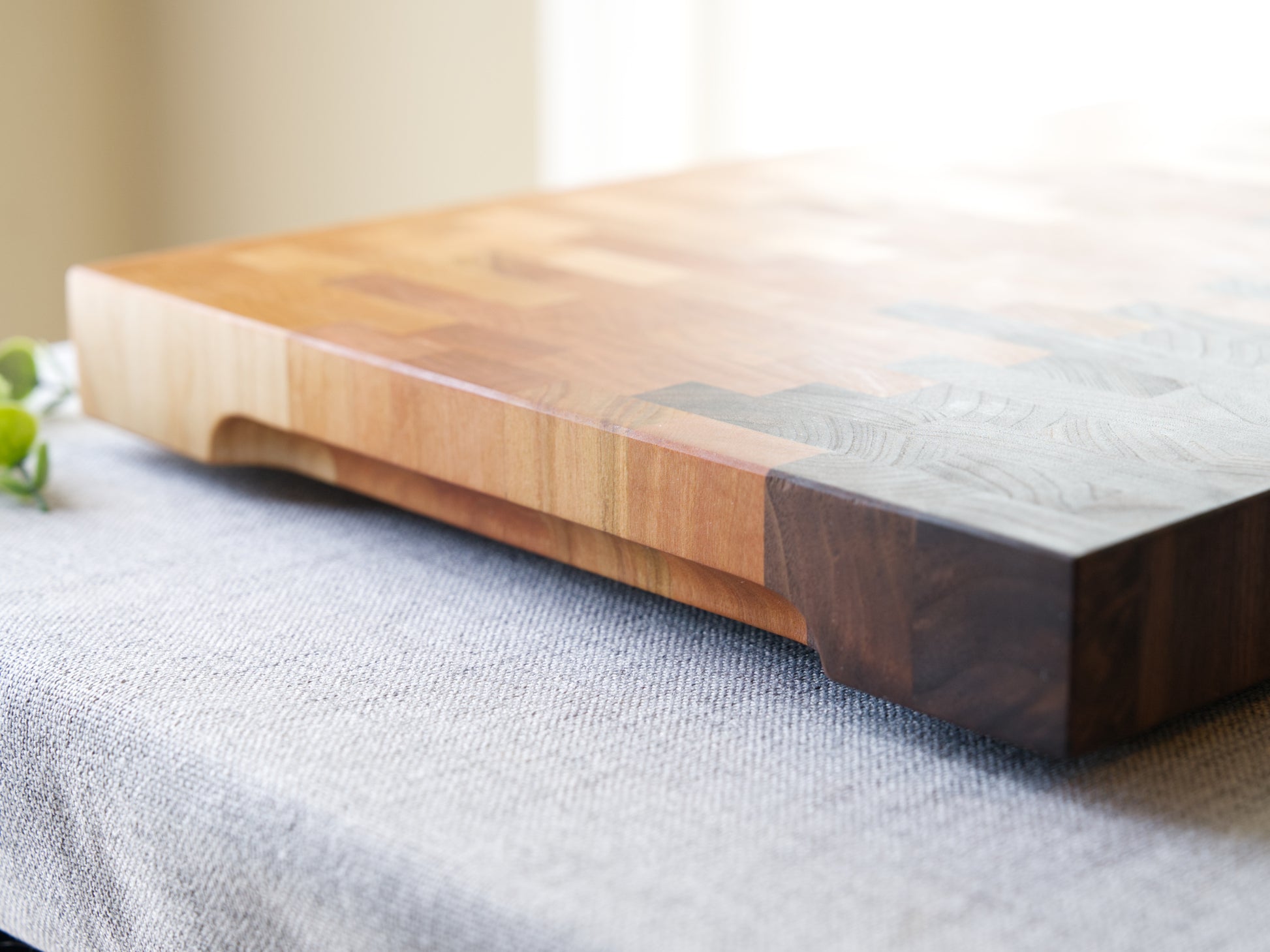 Ombre End Grain Cutting board made from domestic black walnut, maple and cherry. Shown on grey cloth table and is finished with mineral oil and beeswax. Side view is shown to detail the finger grooves